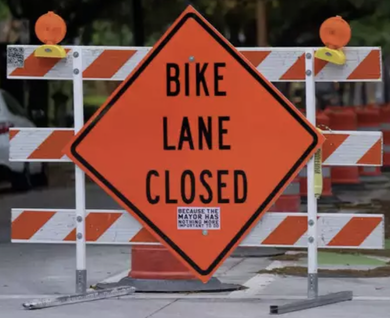 Barrier on Austin Street with sign saying BIKE LANE CLOSED, and bumper sticker added saying BECAUSE THE MAYOR HAS NOTHING MORE IMPORTANT TO DO.